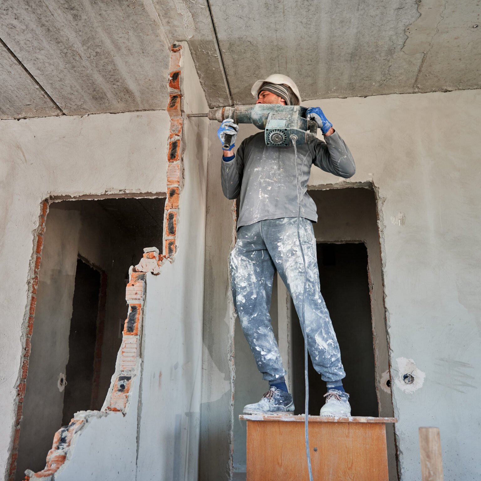 Male worker destroying wall between two rooms with hammer drill